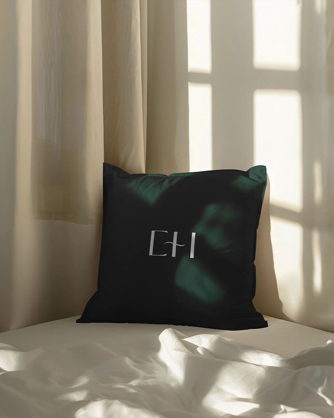 Forest green monogrammed cushion on sunlit white bedding